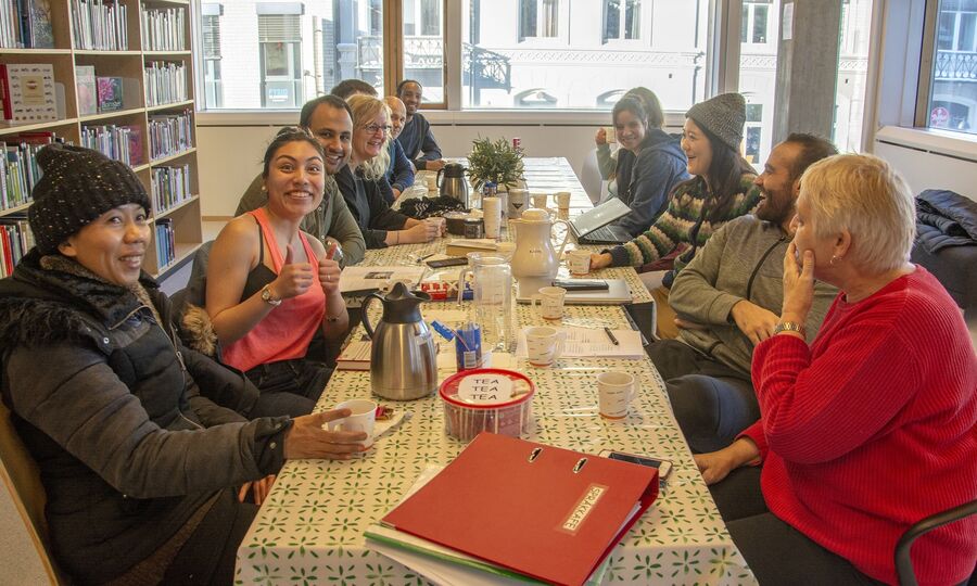 Mennesker sitter rundt et bord og prater sammen og smiler